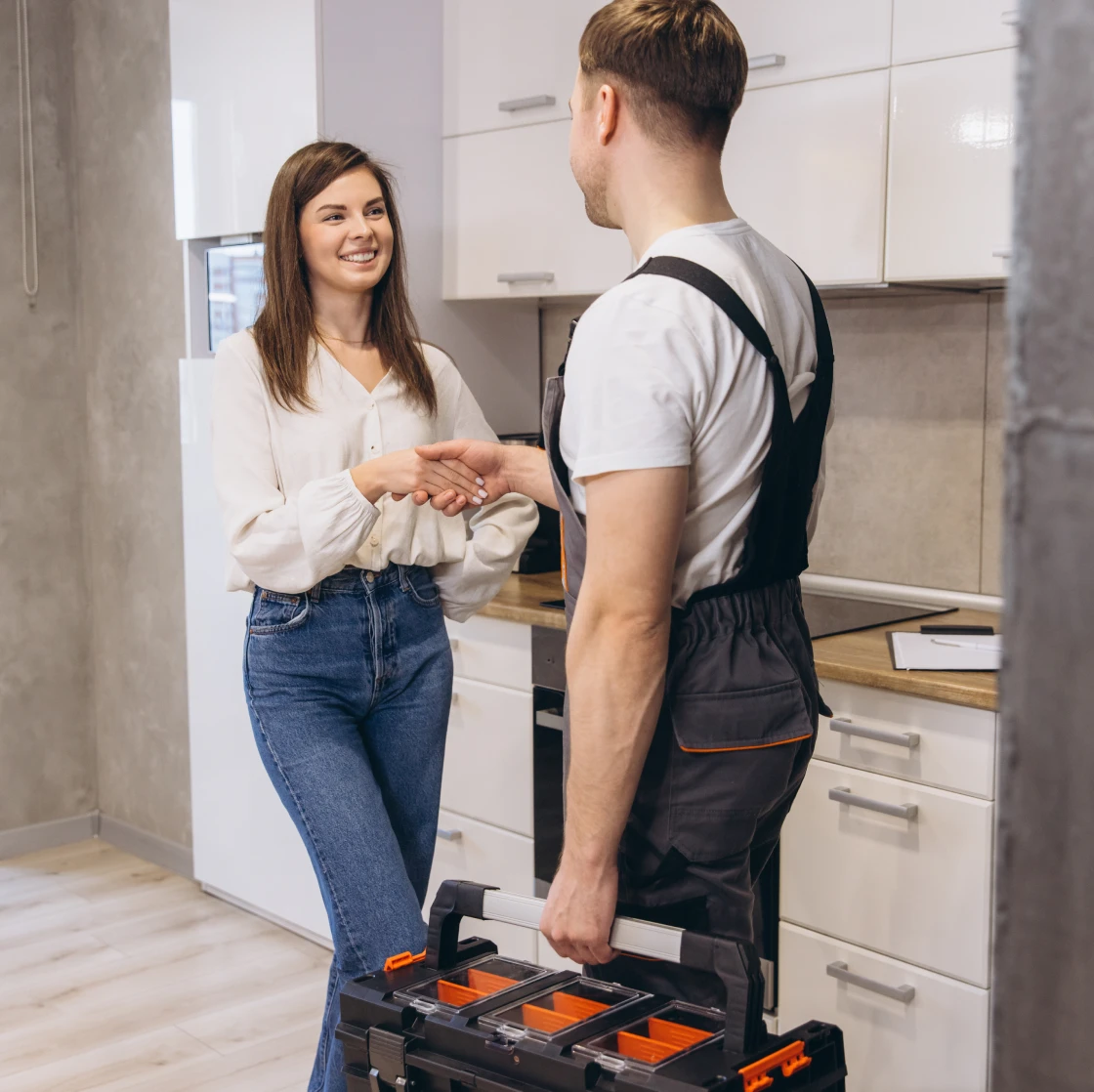 Woman and repairman shaking hands in kitchen.